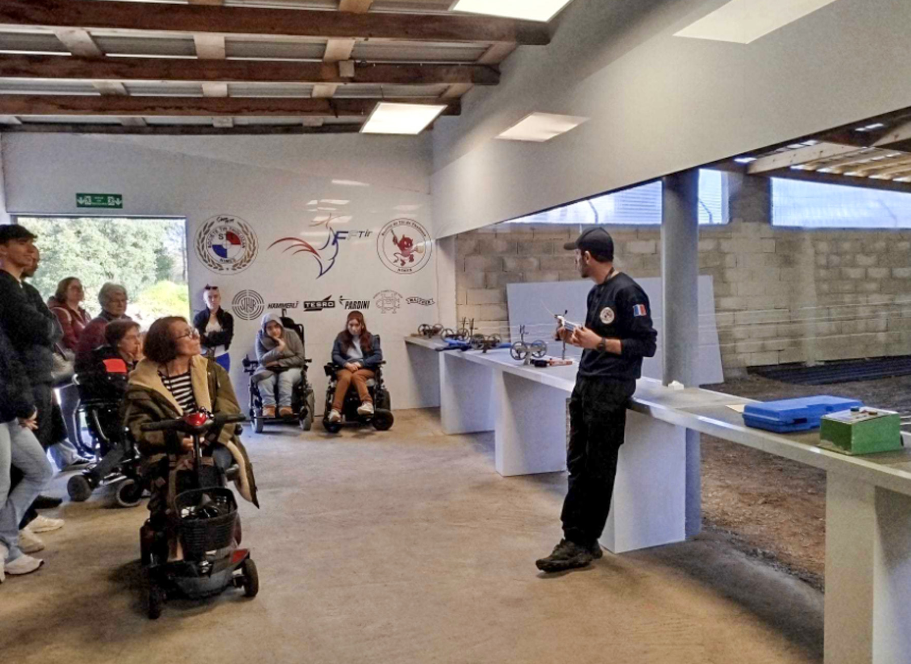 Initiation au tir sportif Moniteur de tir sportif expliquant les consignes de sécurité à un groupe incluant des personnes en situation de handicap.
