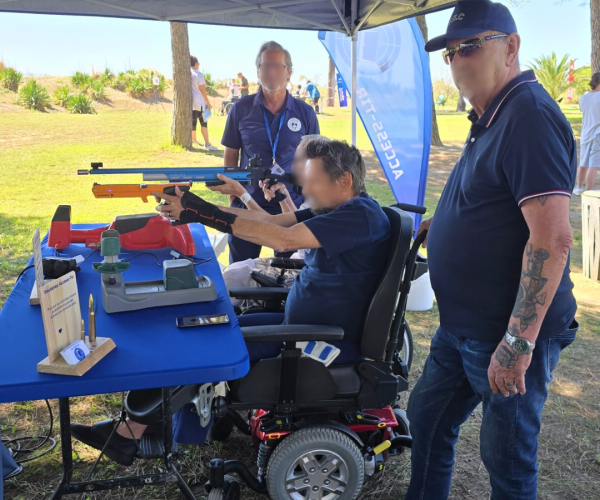 Participant en fauteuil roulant découvrant le tir sportif adapté avec un pistolet laser accompagné par les bénévoles d'Access Tir.